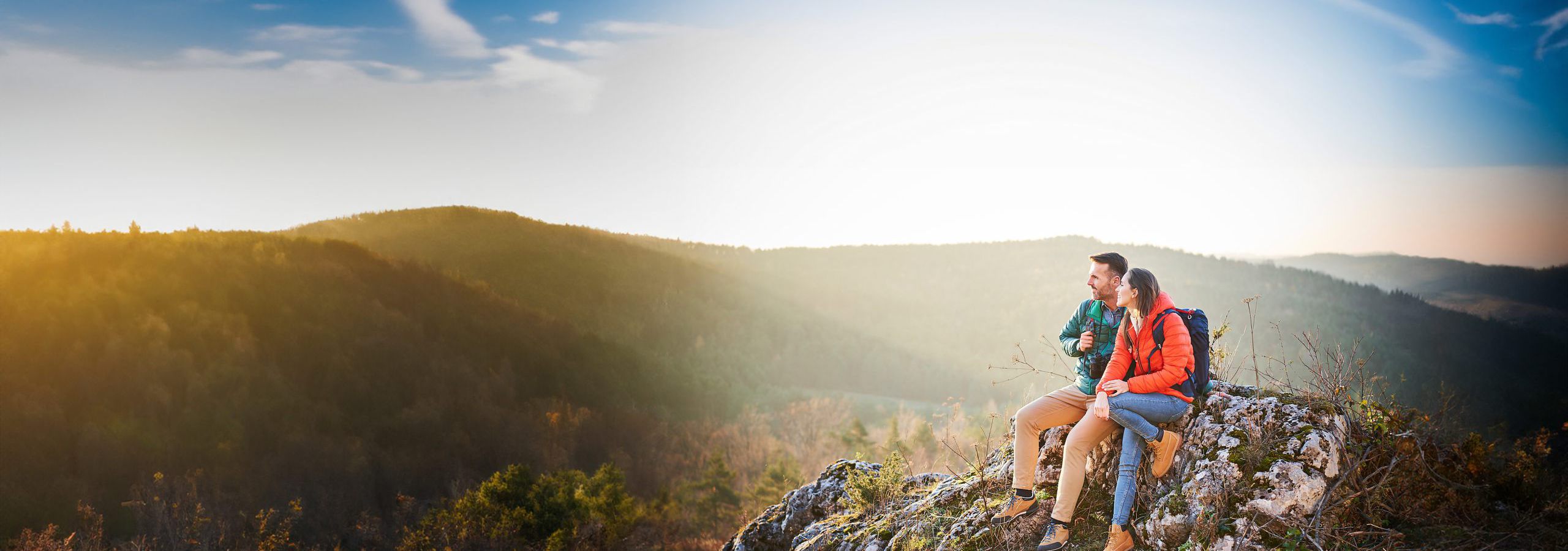 Ein paar sitzt auf einem Gipfel und genießt den Ausblicke auf die umliegenden Berge