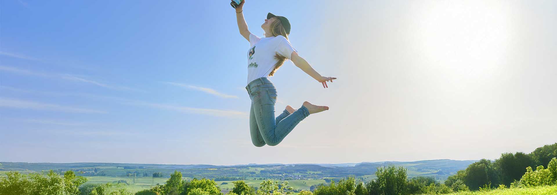 Frau springt in die Luft und hält eine Förster Alkoholfrei Hell von Gampertbräu in der Hand